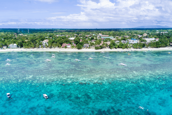 aerial view of turquoise green water, blue sky, and white sand beach