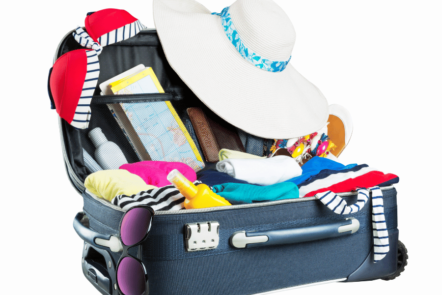 an open luggage filled with beach essentials like a hat, swim wear, sun block, lots of shirts, a map, a sunglass and a wallet