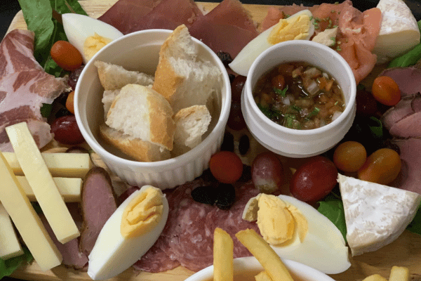 various foods like salami, bread, dips, cheese sticks, french fries, boiled egg, thinly sliced meat, some grapes and vegetables on a plate