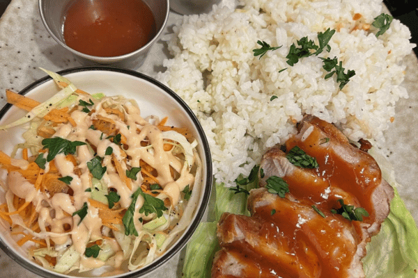 some white rice with slices of pork topped with a special brown sauce. with salad on the side with some dressing. and an extra serving of sauce for the pork
