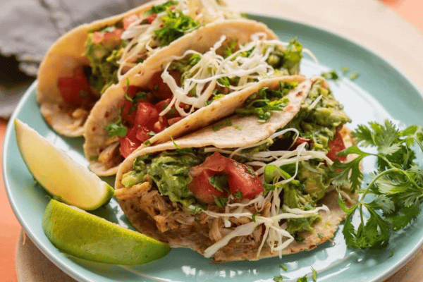 chikcen tacos with vegetable garnish, cilantro, and 2 wedges of lime on the side