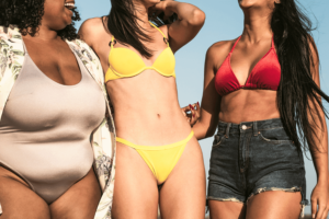 3 ladies wearing beachwear. on the left wearing 1 piece beige swim suit, on the middle wearing 2 piece yellow swimsuit, on the right wearing a two piece red swim suit with a short jeans on top