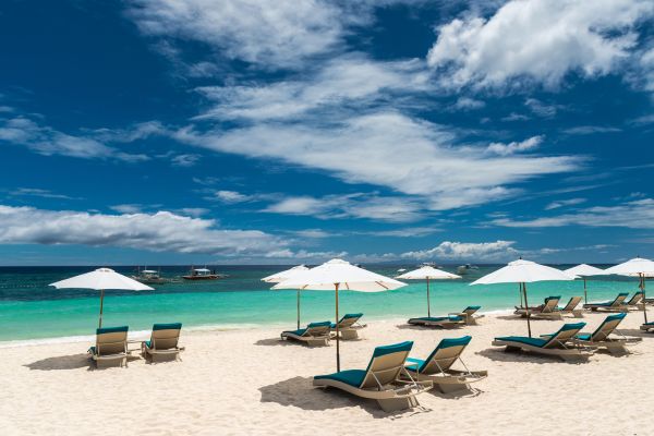 beach umbrellas and lounges on a white sand beach facing the turquoise green ocean under the clear blue sky