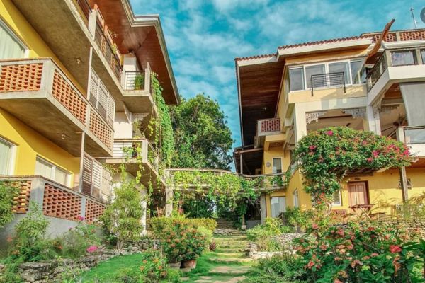a walkway surrounded by greeneries and a view of the hotels on both side of the walkway all under the blue sky