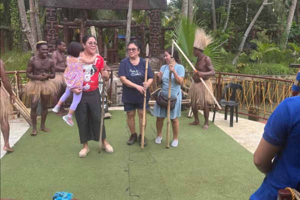 a family with the mother carrying her daughter andn the grandmothers on the right side all carrying spears with the tribes people