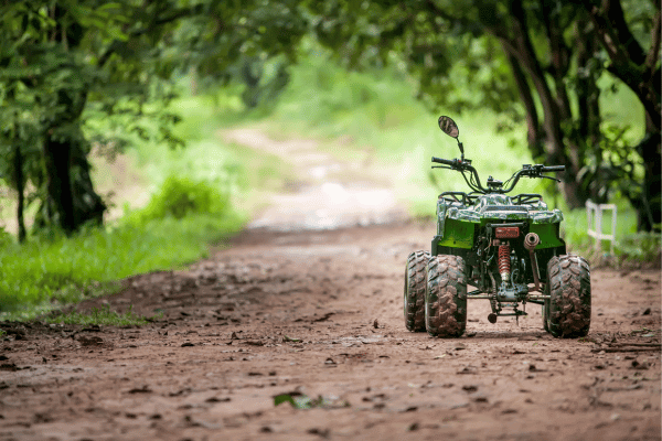 green atv on a muddy road surrounded by grass and trees