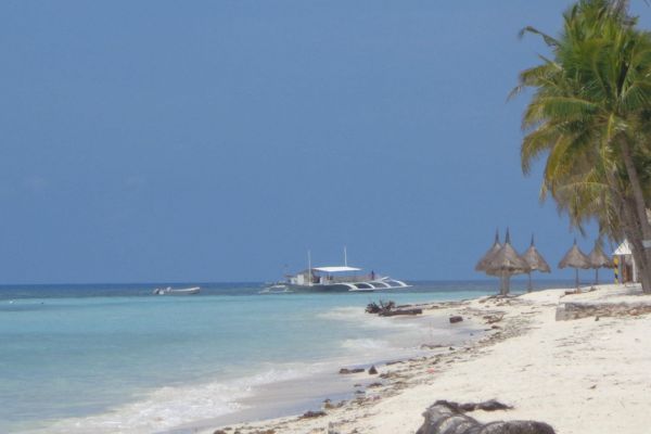 rocky white beach on the right with the view of the sea on the left and a small boat and some cottages not far away