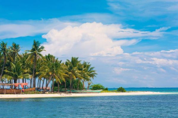 blue water surrounding a white sand beach with lots of palm trees on it all under the blue sky with some huge white clouds
