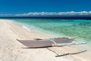 white sandbar on the left, turquoise green sea on the right, with a white boat right in the middle all under the clear blue sky with some white clouds floating far away