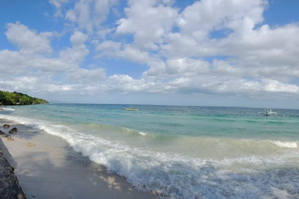 white beach getting hit by the waves of turquoise green ocean creating white bubbles under the blue sky with lots of white clouds