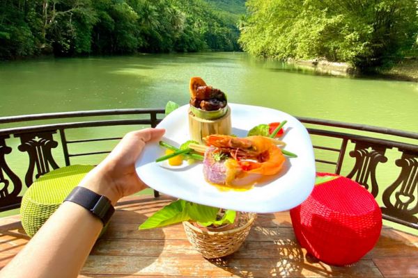 a hand holding a plate with shrimp and salad with the loboc river and the boat's deck on the background