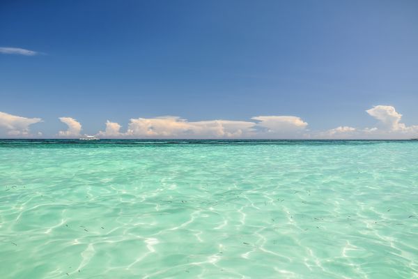 turquoise green clear water with the light reflecting off of it under the clear blue sky with a couple of white clouds far in the horizon