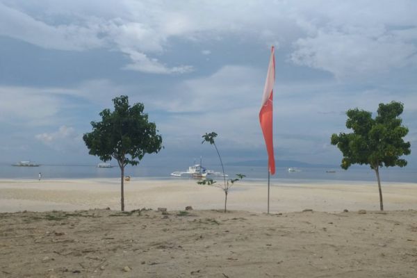 a white beach with a local either on either side and a red and white flag in the middle with a couple of boats not far away under a cloudy sky