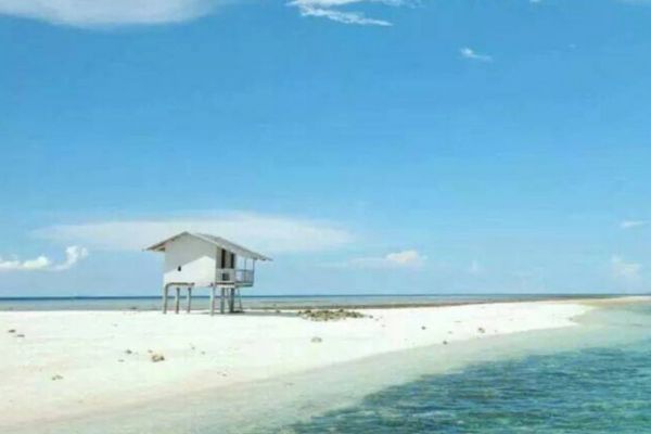 a white sandbar stretching as far as the eye can see with a small white house almost in the middle of the sandbar under the clear blue sky with the ocean on the right side