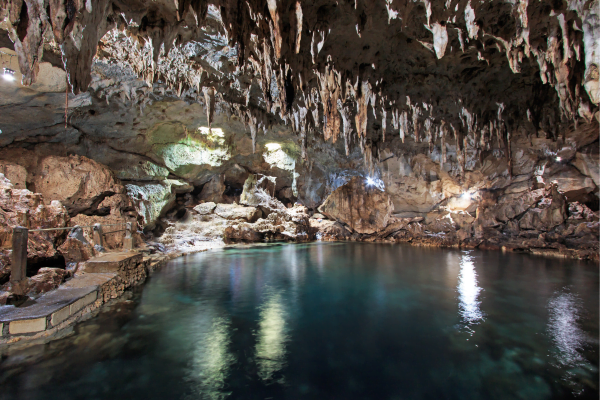 inside a cave with stalactites and stalagmites with a clear lagoon in the middle