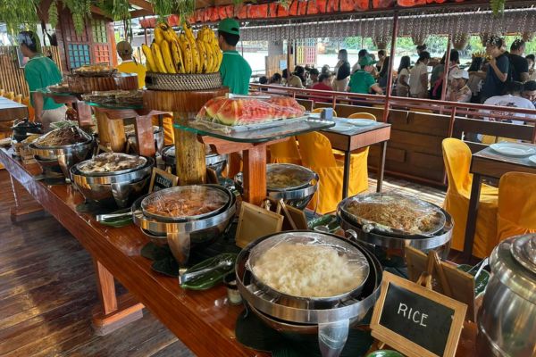 different local dishes like white rice, noodles, fish, and fresh fruits like banana, watermelon all laid out neatly on the table of the floating restaurant