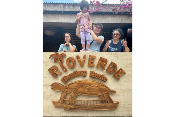 a family with the father holding his daughter by the waist, grandmothers on both sides with the rio verde floating restaurant name and logo in front