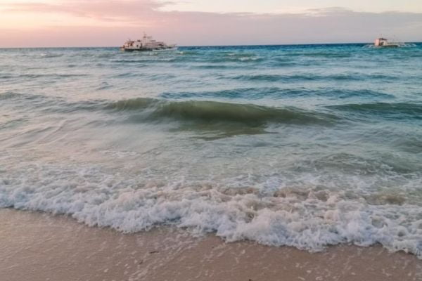blue ocean splashing waves on the shite sand under the pink sky