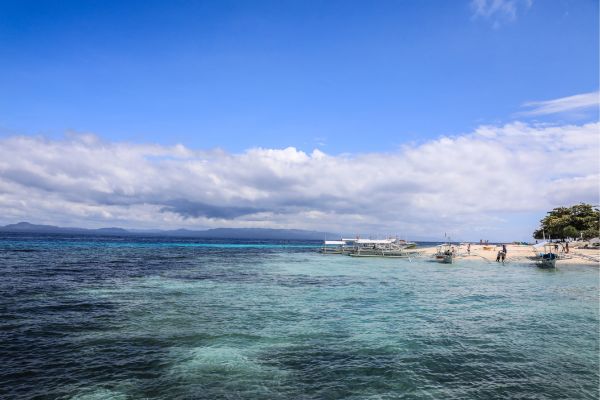 turquoise green water under the blue sky with some white clouds. and the white beach with some boats visible on the right side