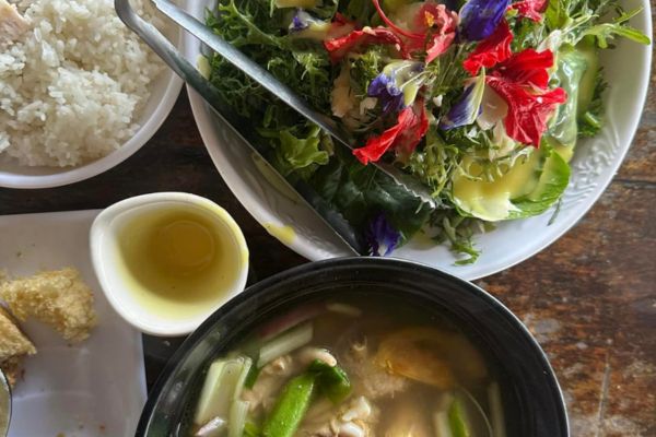 pork soup in a bowl, salad greens in another bowl and a cup of rice all on a table