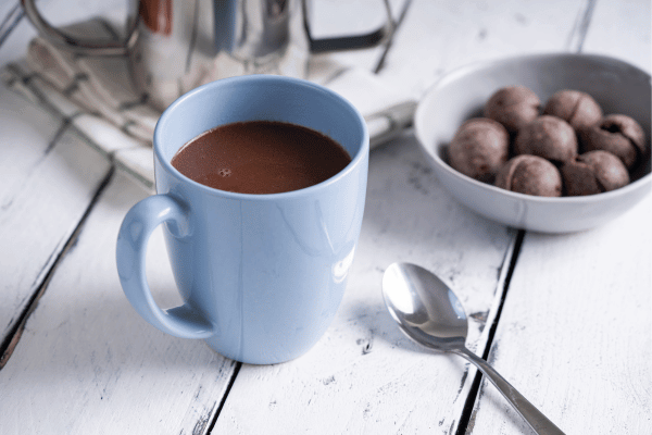 hot dark chocolate, also known as tablea, in a cup with a spoon on the side and other ball shaped sweets