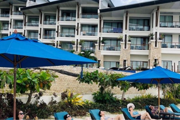 front view of the bellevue hotel with women lounging in the beach under beach umbrellas