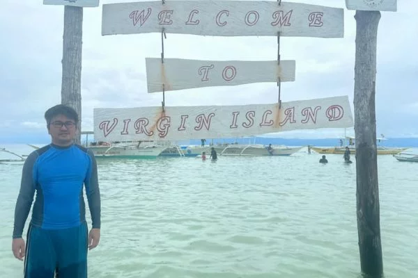 me, male wearing glasses and blue rash guard standing in front of a sign saying welcome to virgin island