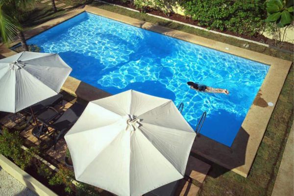 top view of a woman swimming in a swimming pool with white beach umbrellas on the lower left of the screen