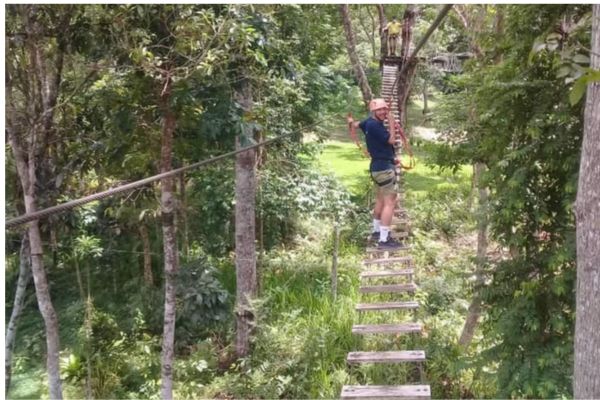 a man crossing a wooden hanging bridge with a big gap between the steps