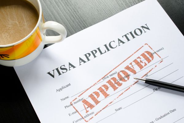 a cup of coffee and a visa application form with an Approved mark and a pen on a table