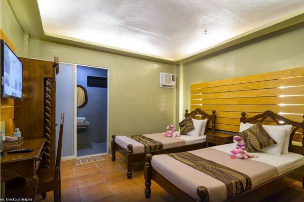 a hotel room with 2 double size bed, a flat screen tv and a table, an airconditioning unit, an open door showing the shower room