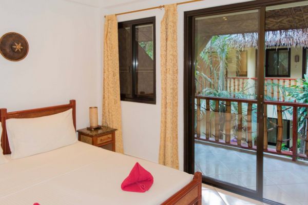 a hotel room with a queensize bed in white sheet, a glass window and a glass door a veranda