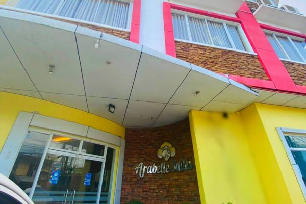 the front entrance of a hotel with the name arabelle suites on the wall. with the second floor visible with the rooms' border painted in red surrounding the glass windows.the ground floor walls are almost all yellow