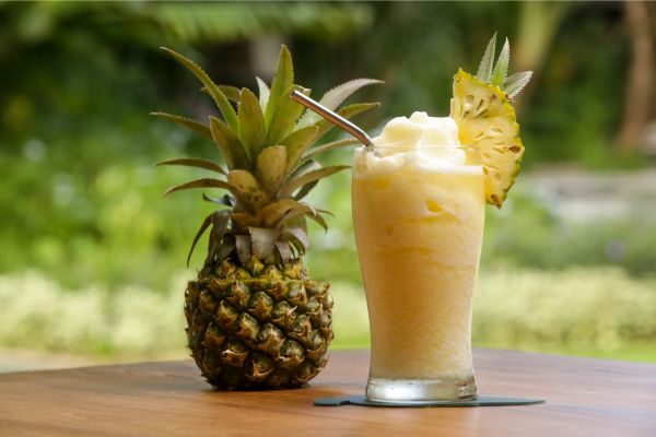 a pineapple on the left and a pineapple smoothie in a glass on the right