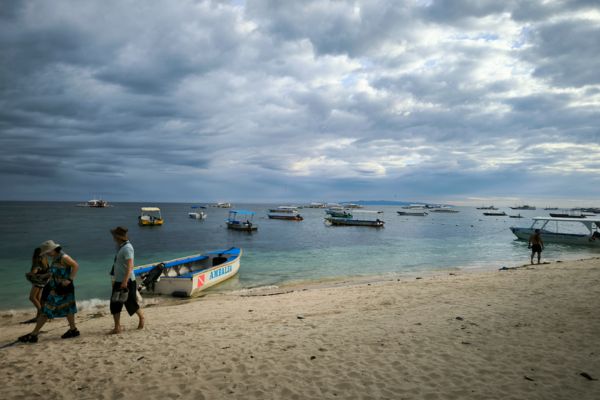 white beach sand bar and the ocean under the dark cloudy sky with some people walking on the beach
