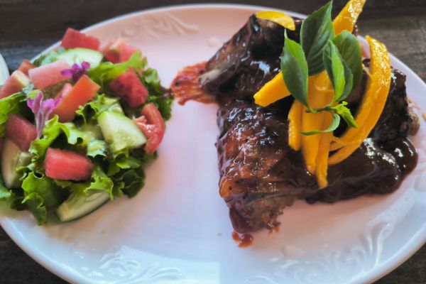grilled spare ribs with mango strips and a side of green salad on a white plate