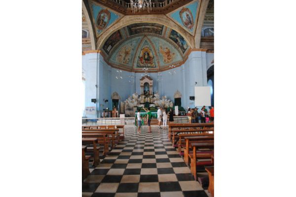 church aisle with black and white tiles, with traditional church chairs and artwork on the ceiling and some people inside the church