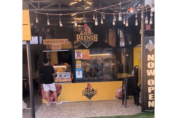 roasted chicken shop that reads Paengs with a customer buying their famous roasted chicken