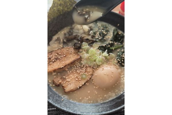 a tonkotsu ramen with egg, pork belly slices, nori, vegetables, sesame seeds