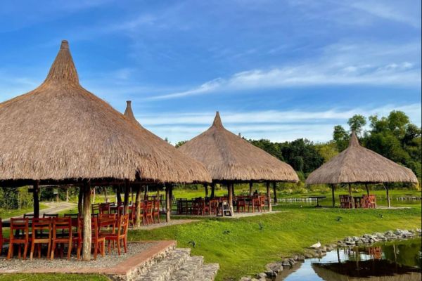 farm with cottages that look like nippa hut with a creek all under the blue sky